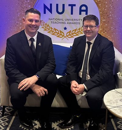 Two men in suits sitting on a couchAI-generated content may be incorrect.